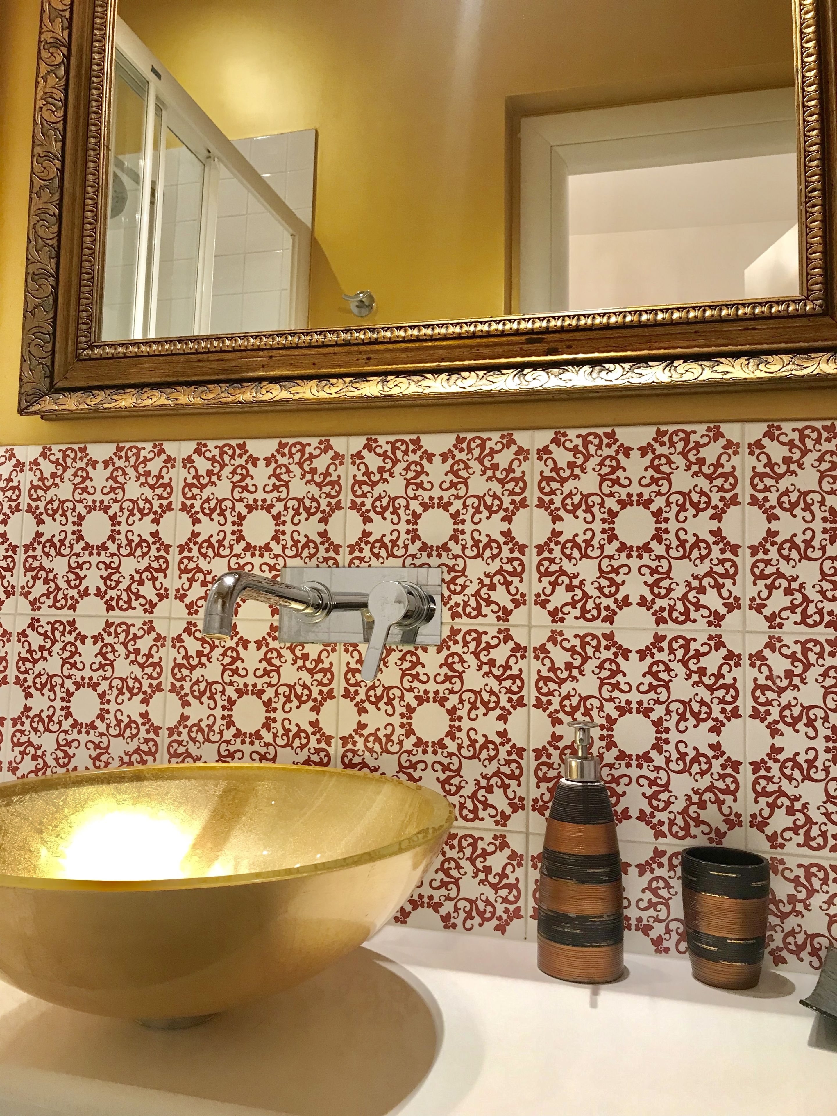 Ein Badezimmer mit einer goldfarbenen Waschschale, einem Spiegel mit aufwendigem Rahmen und gemusterten Fliesen.