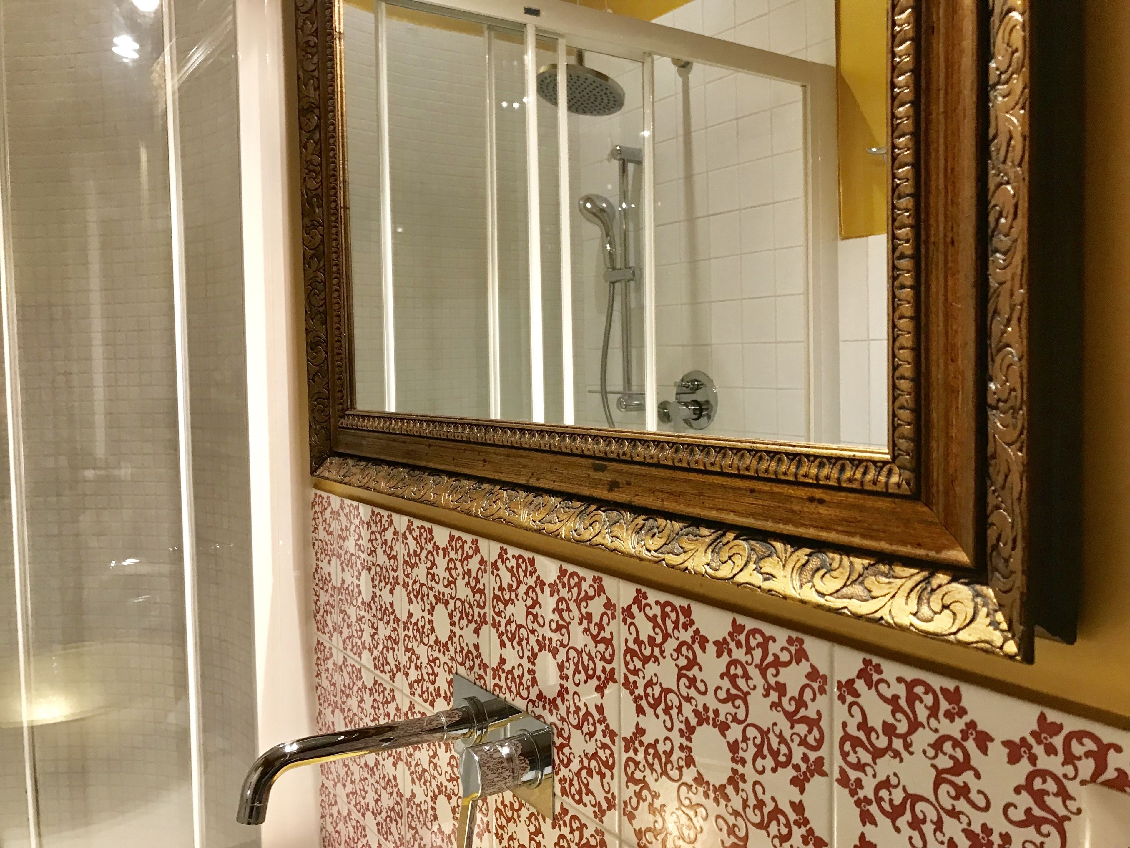 A bathroom with a shower, a mirror with an ornate frame, and patterned tiles.