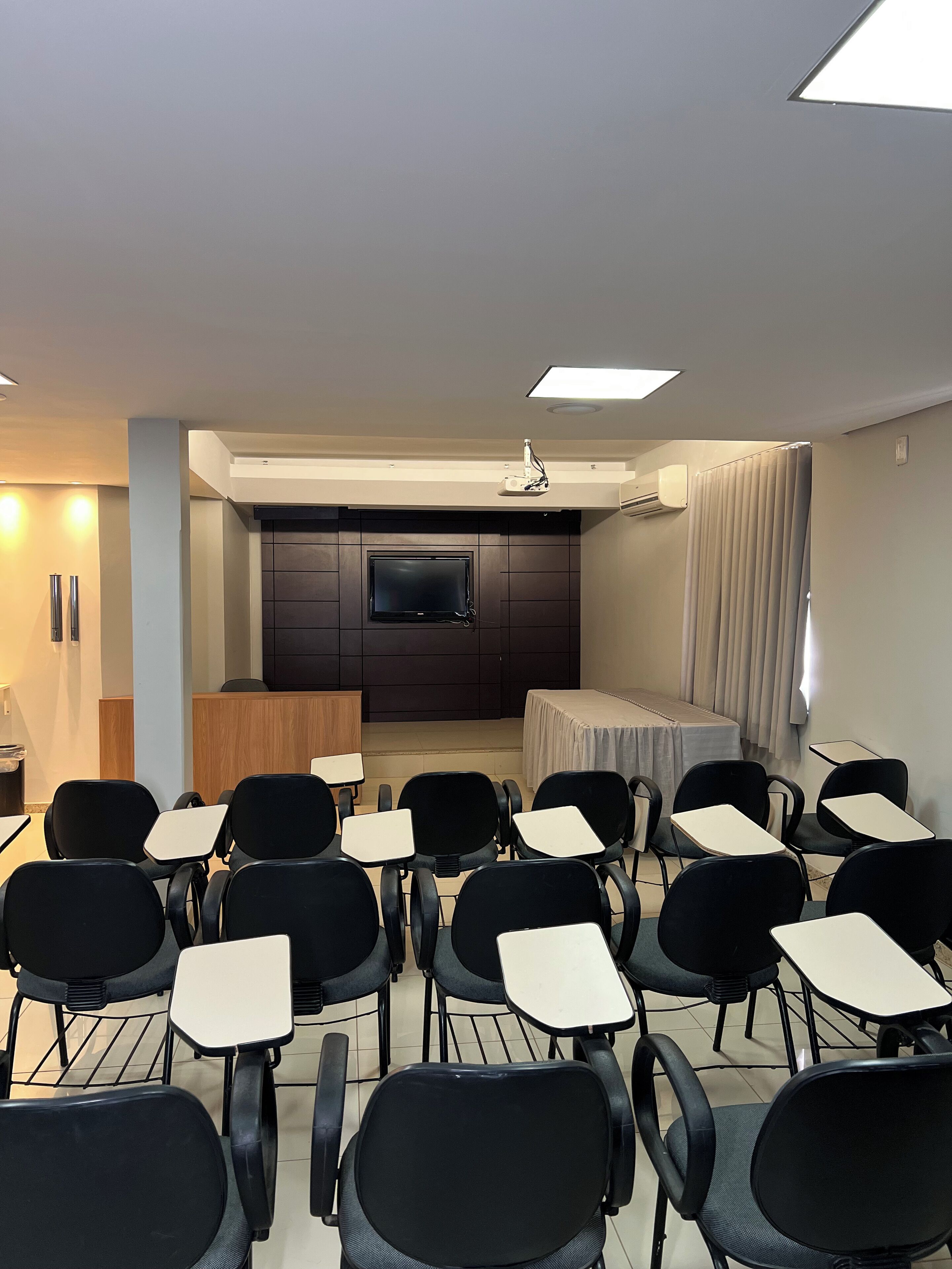 A conference room with rows of chairs and tables, a large screen, and a podium.