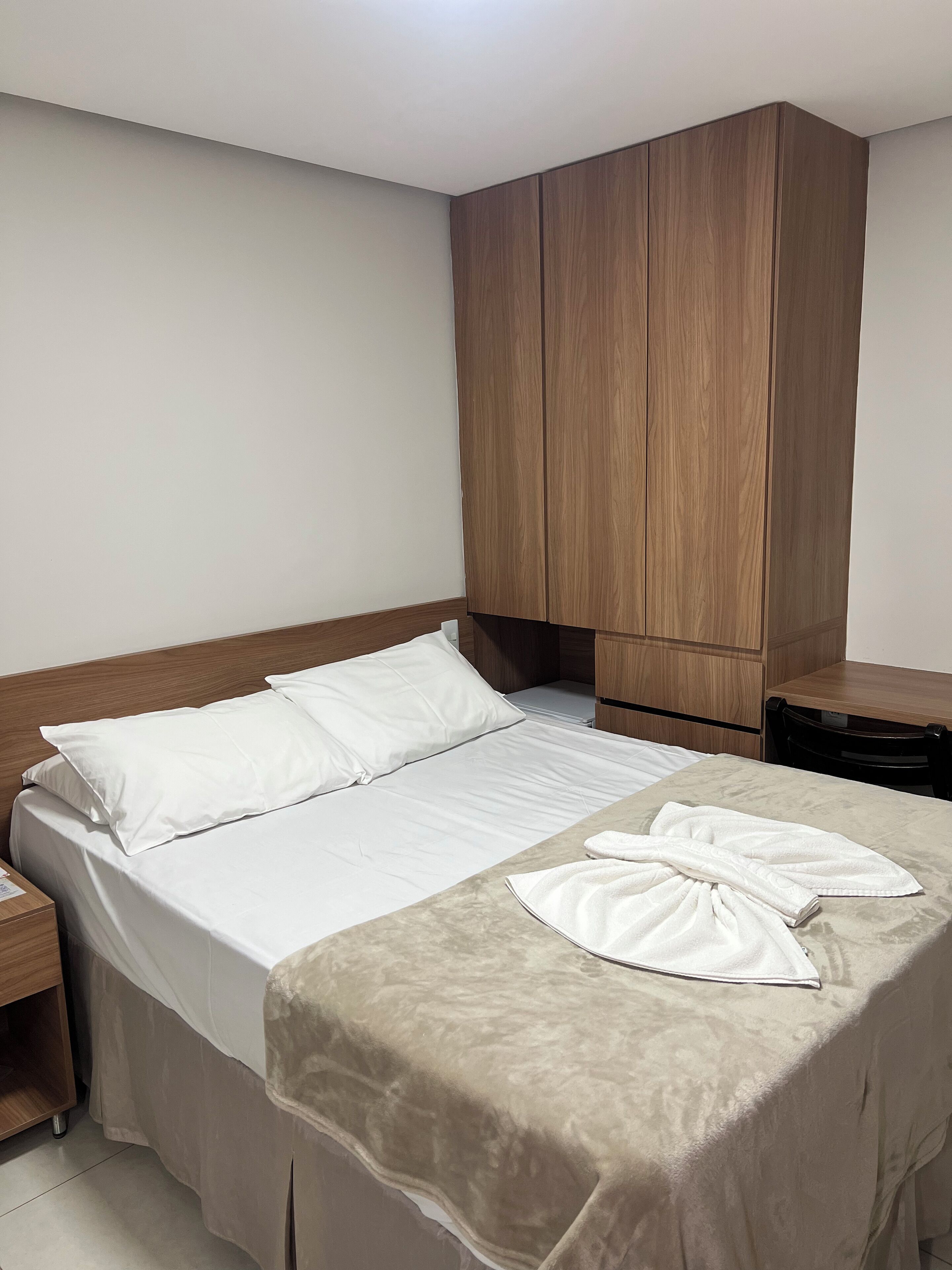 Un lit bien fait, avec des draps blancs, une tête de lit en bois et une couverture beige.