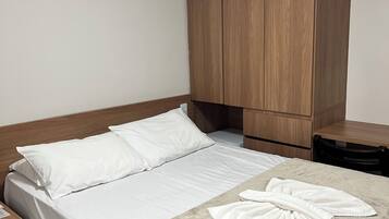 Un lit bien fait, avec des draps blancs, une tête de lit en bois et une couverture beige.