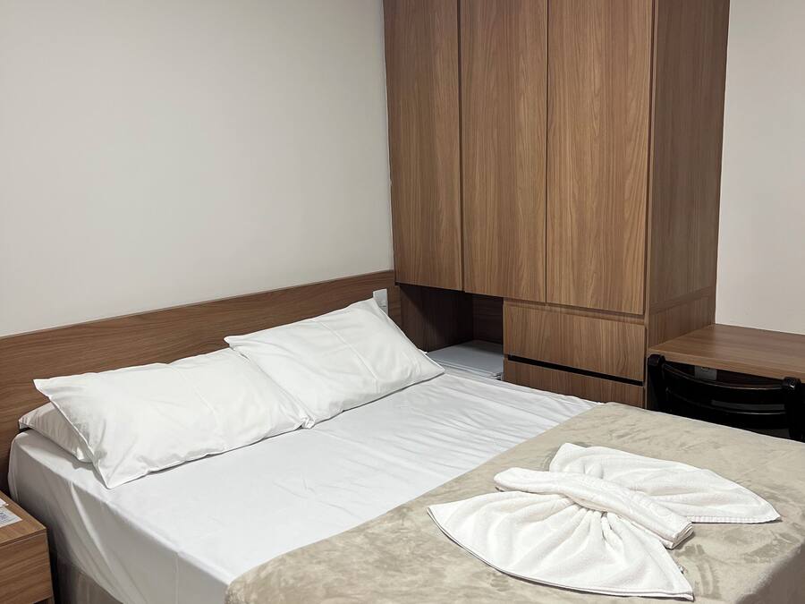 Un lit bien fait, avec des draps blancs, une tête de lit en bois et une couverture beige.