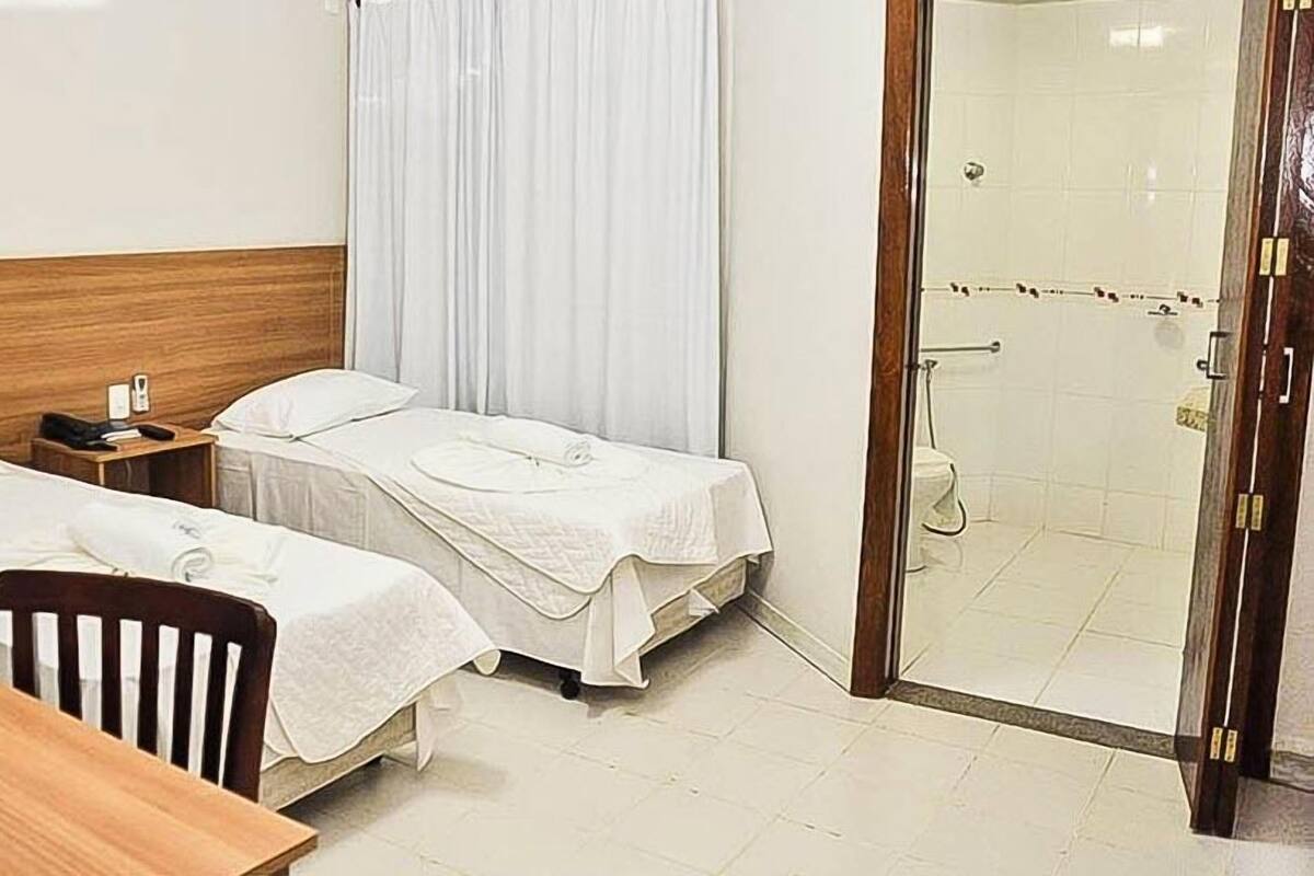 Een hotelkamer met twee bedden, een houten hoofdbord, een klein tafeltje, een nachtkastje en een douche.