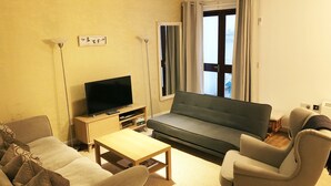 Un salon comprenant un canapé, des fauteuils, une table basse, un téléviseur et une bibliothèque.