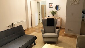 Un salon avec un canapé gris, un fauteuil gris, une table basse en bois et un petit bureau agrémenté d’une plante.