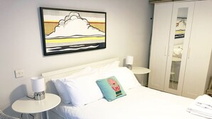 Une chambre d’hôtel comprenant un lit, deux tables de chevet, une lampe, une armoire et une œuvre d’art accrochée au mur.