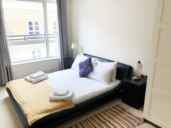 A hotel room with a bed, a nightstand, a lamp, and a view of the outside.