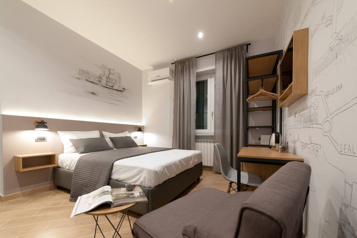 A modern hotel room with a large bed, bedside tables, a desk, a chair, and a map on the wall.