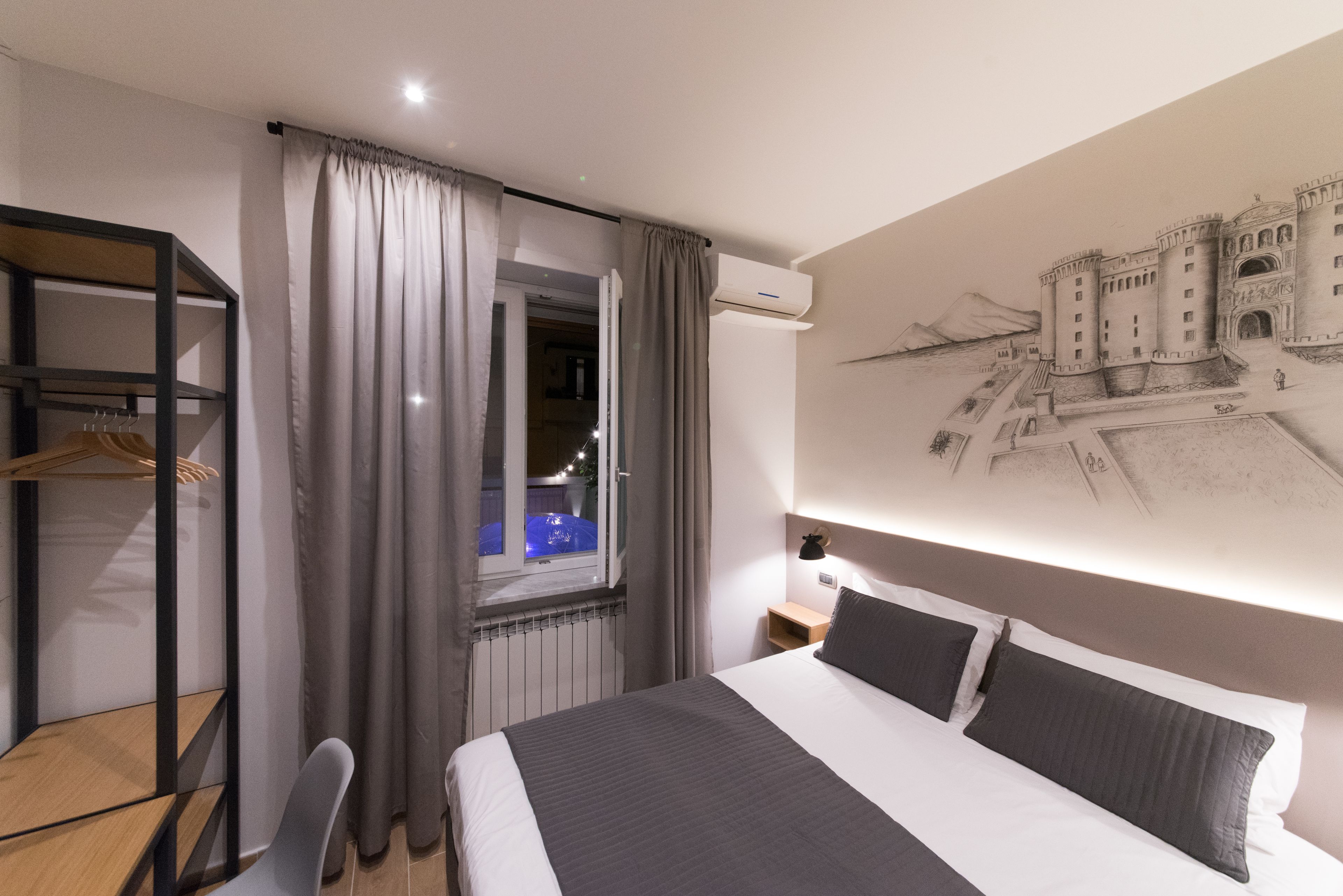 Een moderne hotelkamer met een groot bed, een bureau, een stoel, een kledingkast en uitzicht op een kasteel door een raam.