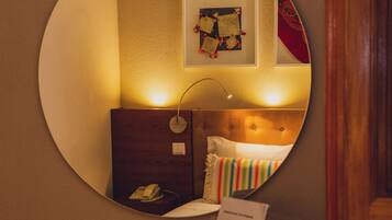 Un espejo circular refleja una habitación con una cama, una mesita de noche con un teléfono y un cuadro colgado en la pared.
