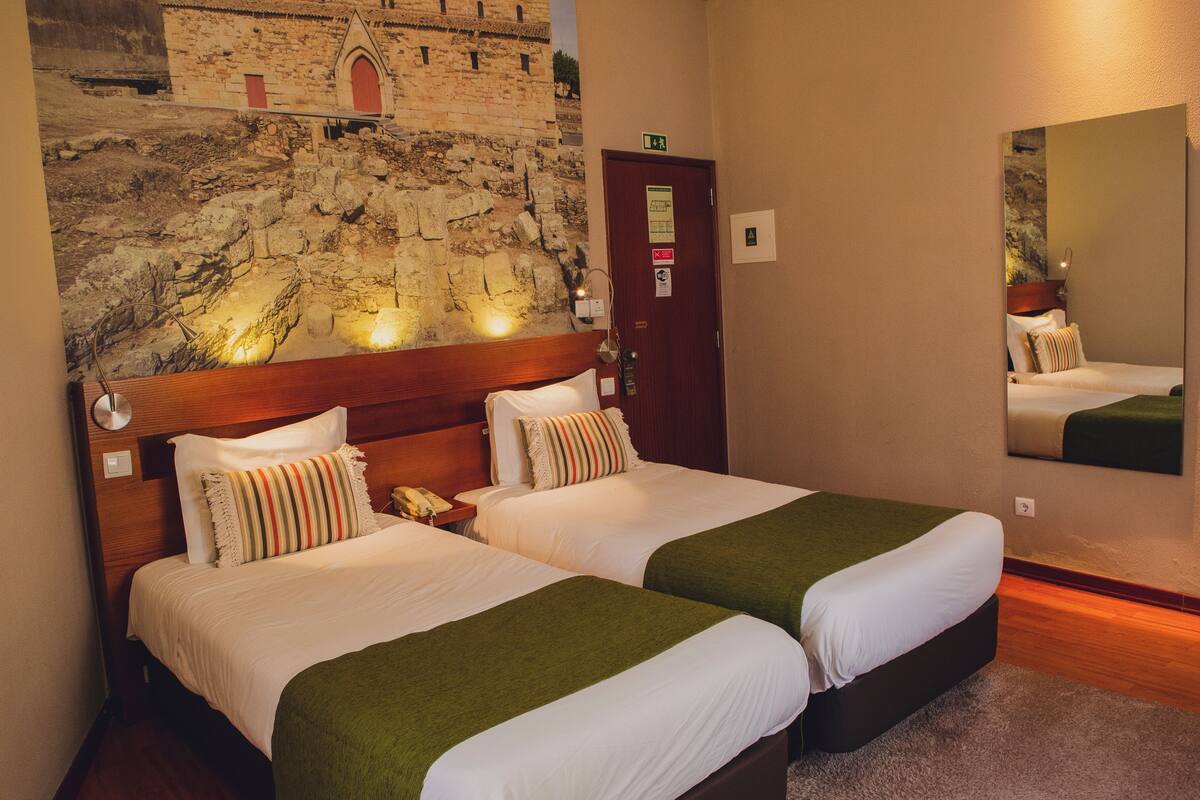 Ein Hotelzimmer mit zwei Betten, einer Wandmalerei aus Stein, einem hölzernen Kopfteil und einer grünen Tagesdecke.