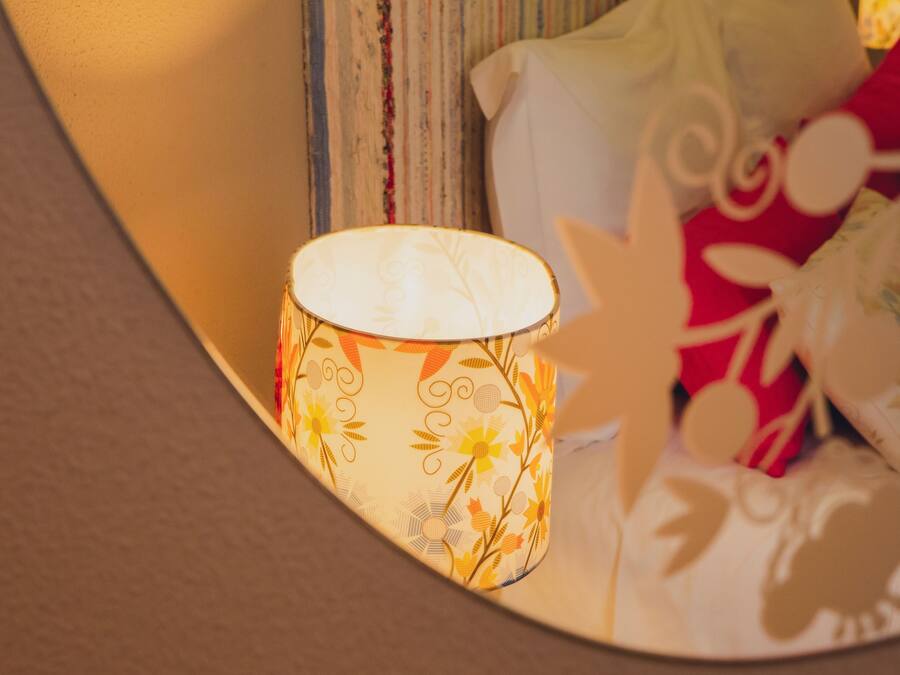 Una lampada con motivo floreale, una tenda a righe e un cuscino con decorazione rossa e bianca.
