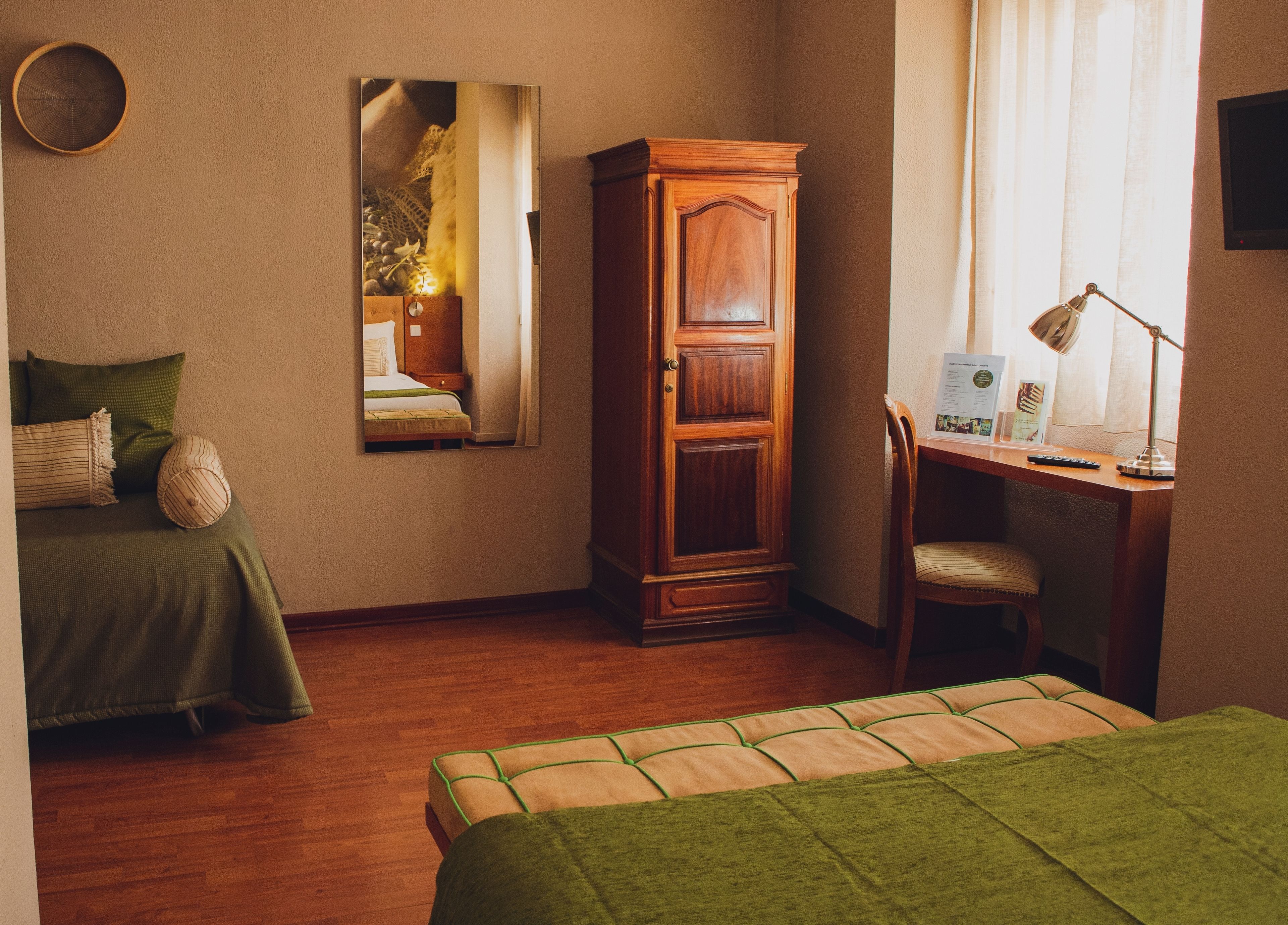 Een kamer met een bed, bureau, stoel, kledingkast en spiegel.