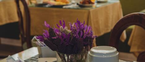 Una mesa de comedor con un jarrón de flores moradas, una taza y un plato de comida al fondo.
