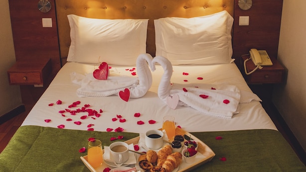 A neatly made bed with a tray of breakfast, swan-shaped towels, and rose petals. - Hotel Império do Rei (Castelo Branco)