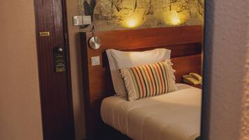 A hotel room with a wooden headboard, a bed with white bedding, a striped pillow, a wall-mounted lamp, and a telephone.