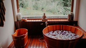 A wooden bathtub filled with water and flowers, a small Buddha statue, and a window with a view of greenery. - Hotel Boutique Quebra-Noz Conforto e Natureza (Campos do Jordão)