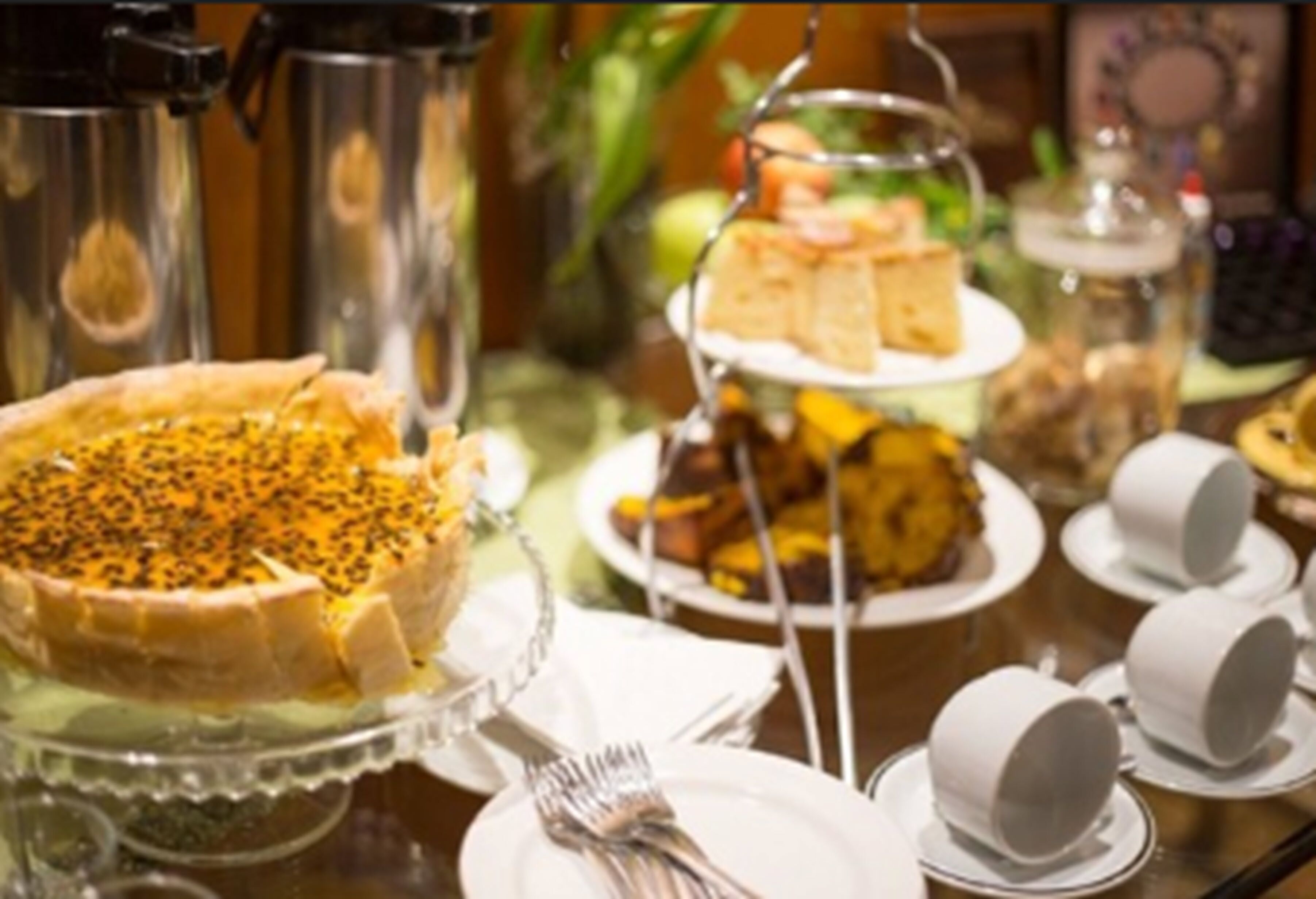 A buffet table with various dishes, including a pie with seeds on top, a cake on a stand, and several cups and plates.