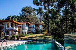 A pool area with a clear view of a building with multiple balconies and a poolside seating area. - Hotel Boutique Quebra-Noz Conforto e Natureza (Campos do Jordão)