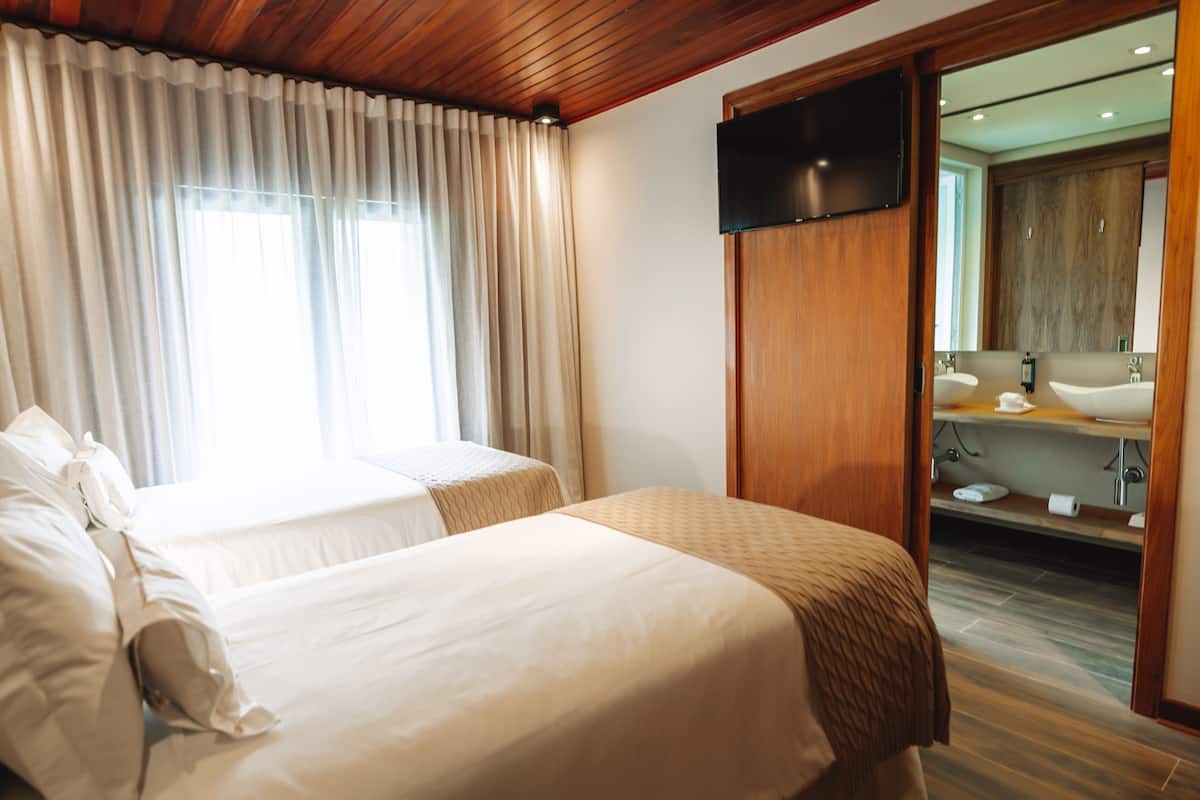 A hotel room with two beds, a television, a bathroom with a mirror, and a wooden ceiling.