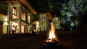 A modern building with a fire pit in the foreground, large windows, and outdoor lighting. - Hotel Boutique Quebra-Noz Conforto e Natureza (Campos do Jordão)