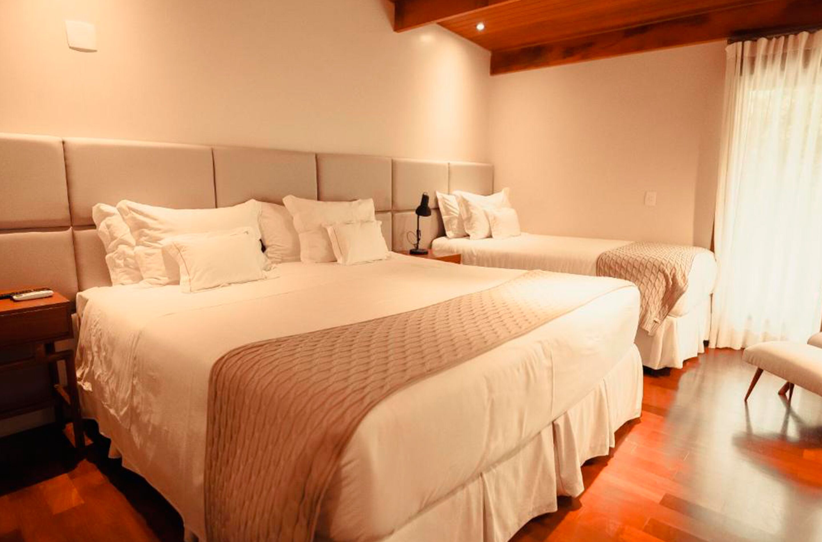 A hotel room with two beds, a bench, and a wooden floor.