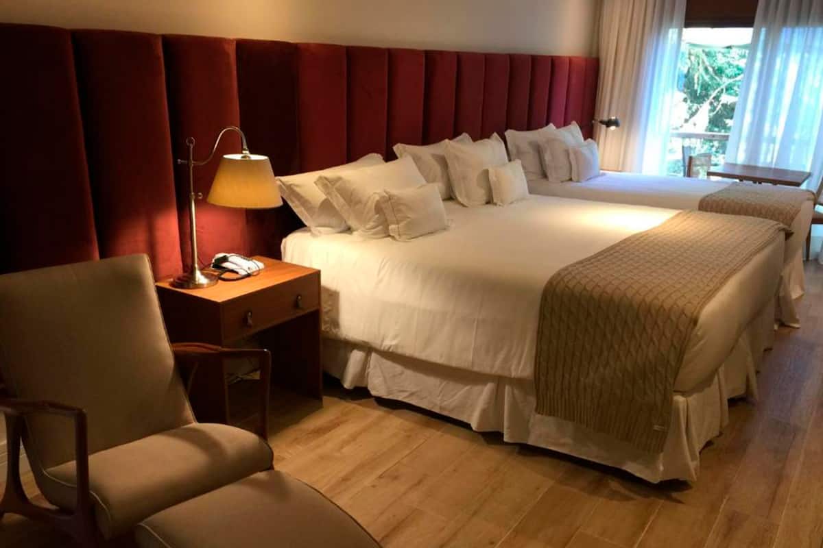 A hotel room with a large bed, a bedside table with a lamp, a chair, and a view of the outdoors.
