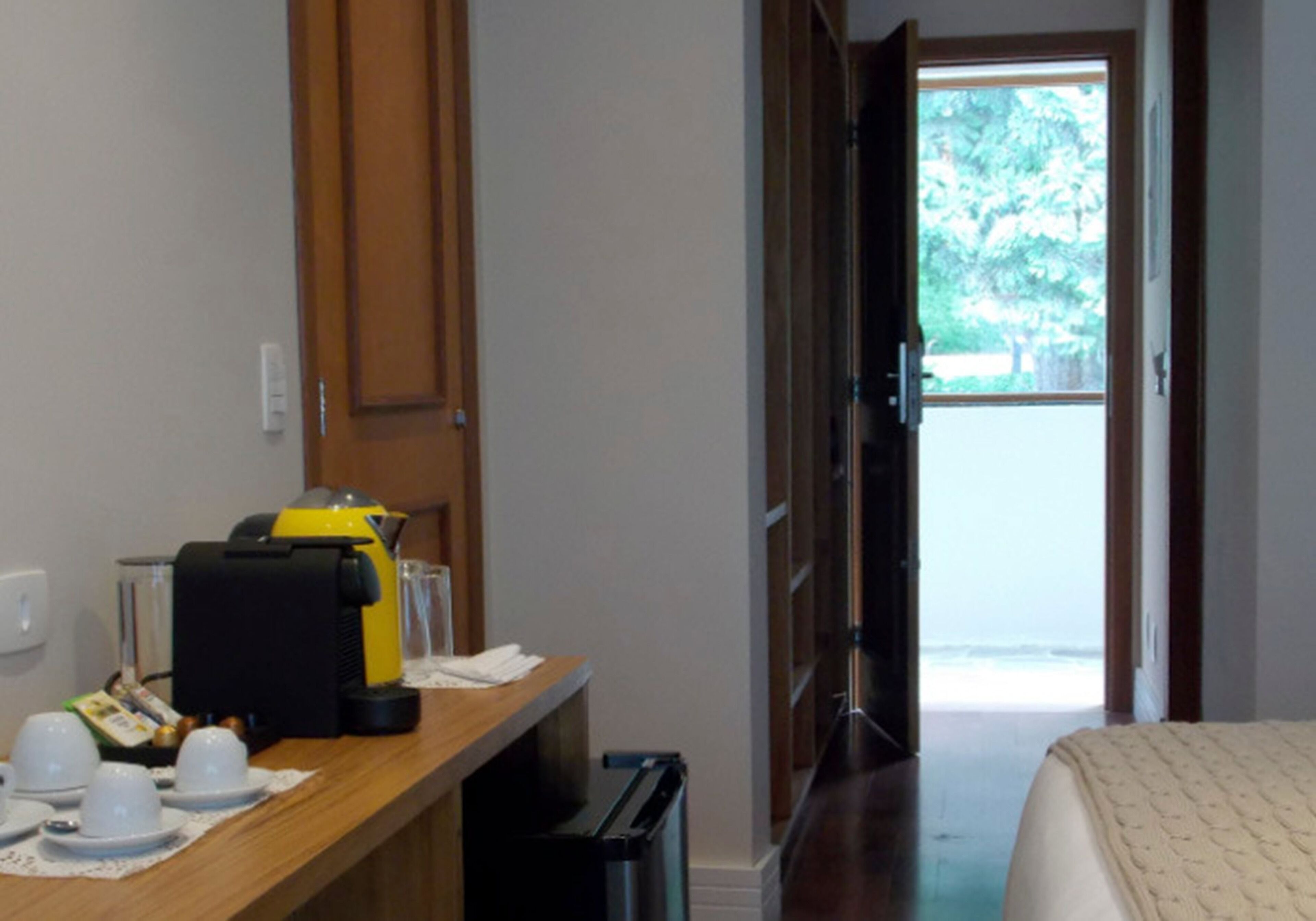 A hotel room with a wooden desk, a coffee machine, and a view of the beach through an open door.