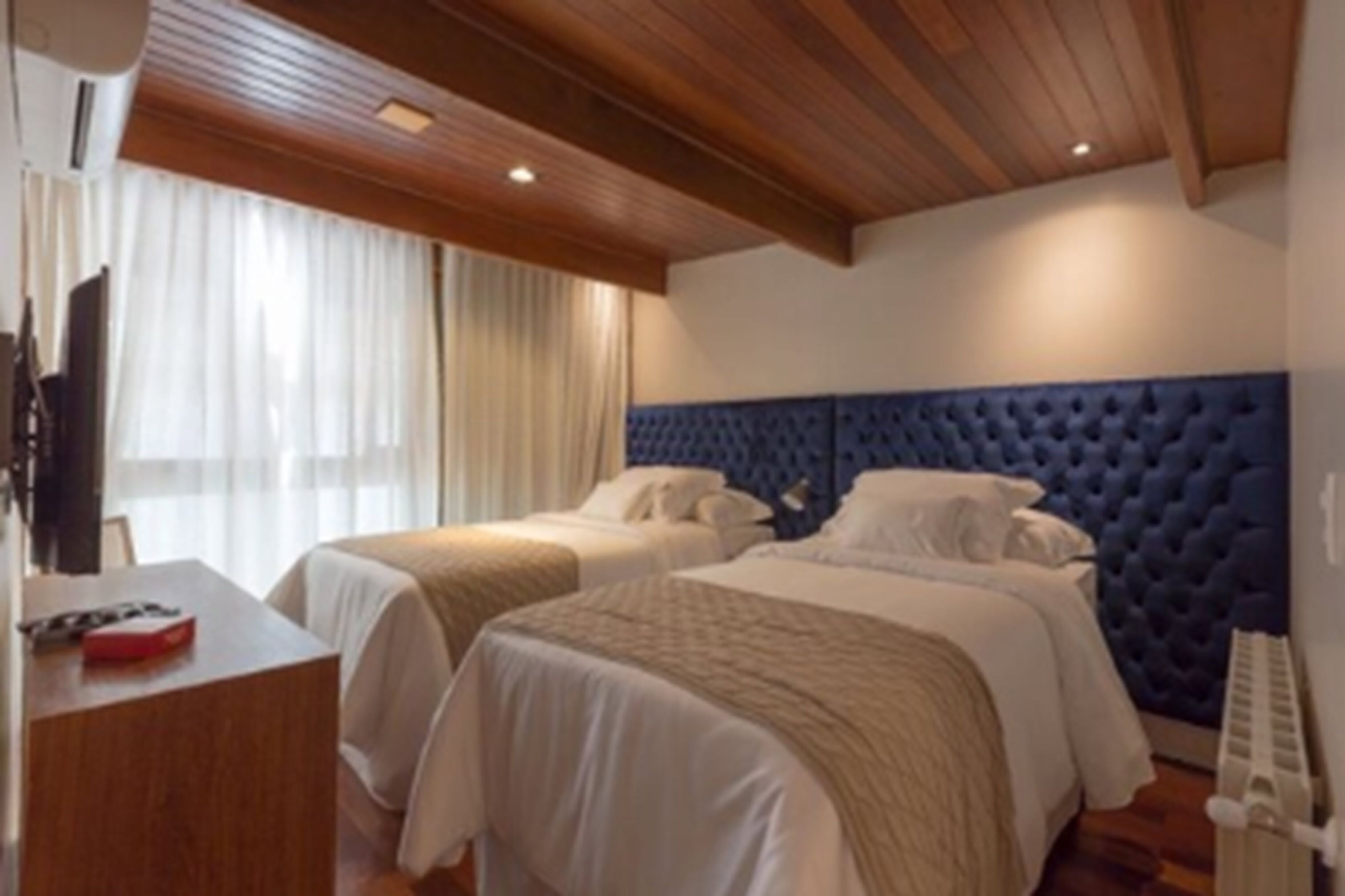 A hotel room with two beds, wooden ceiling, and a desk with a chair.