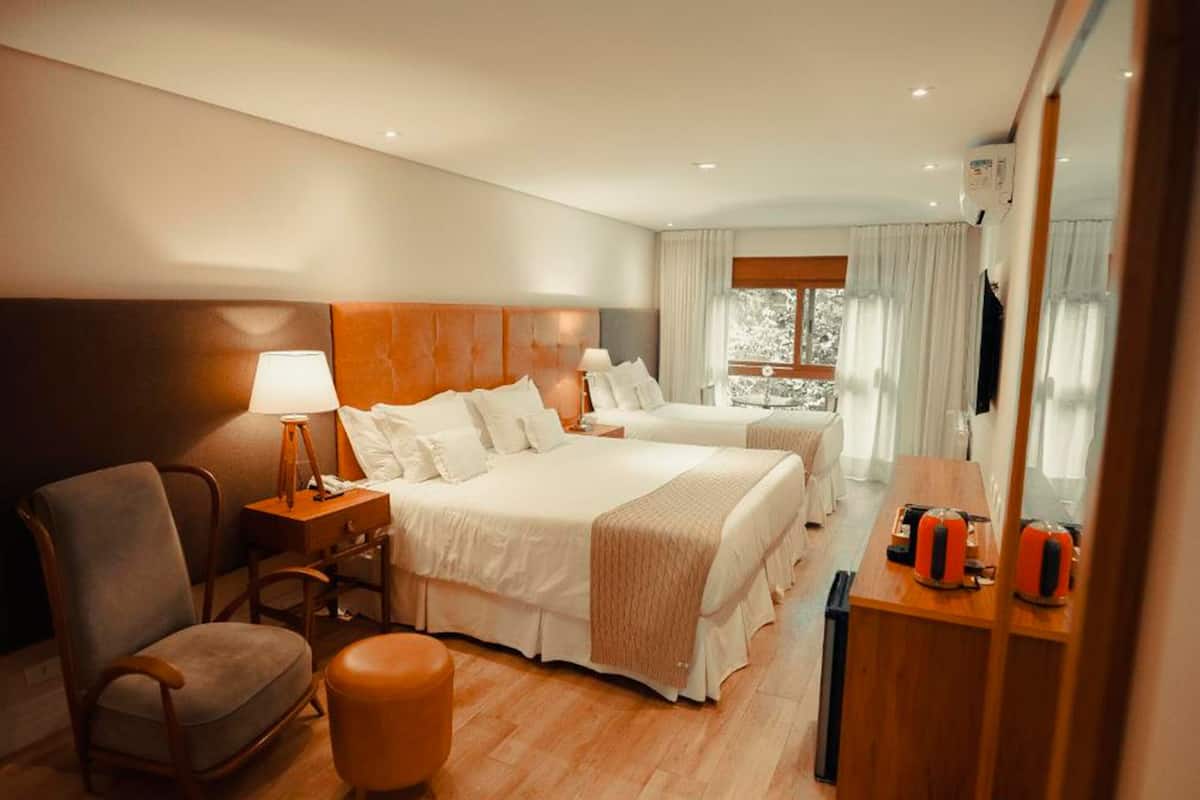 A hotel room with two beds, a chair, a desk, and a mirror.