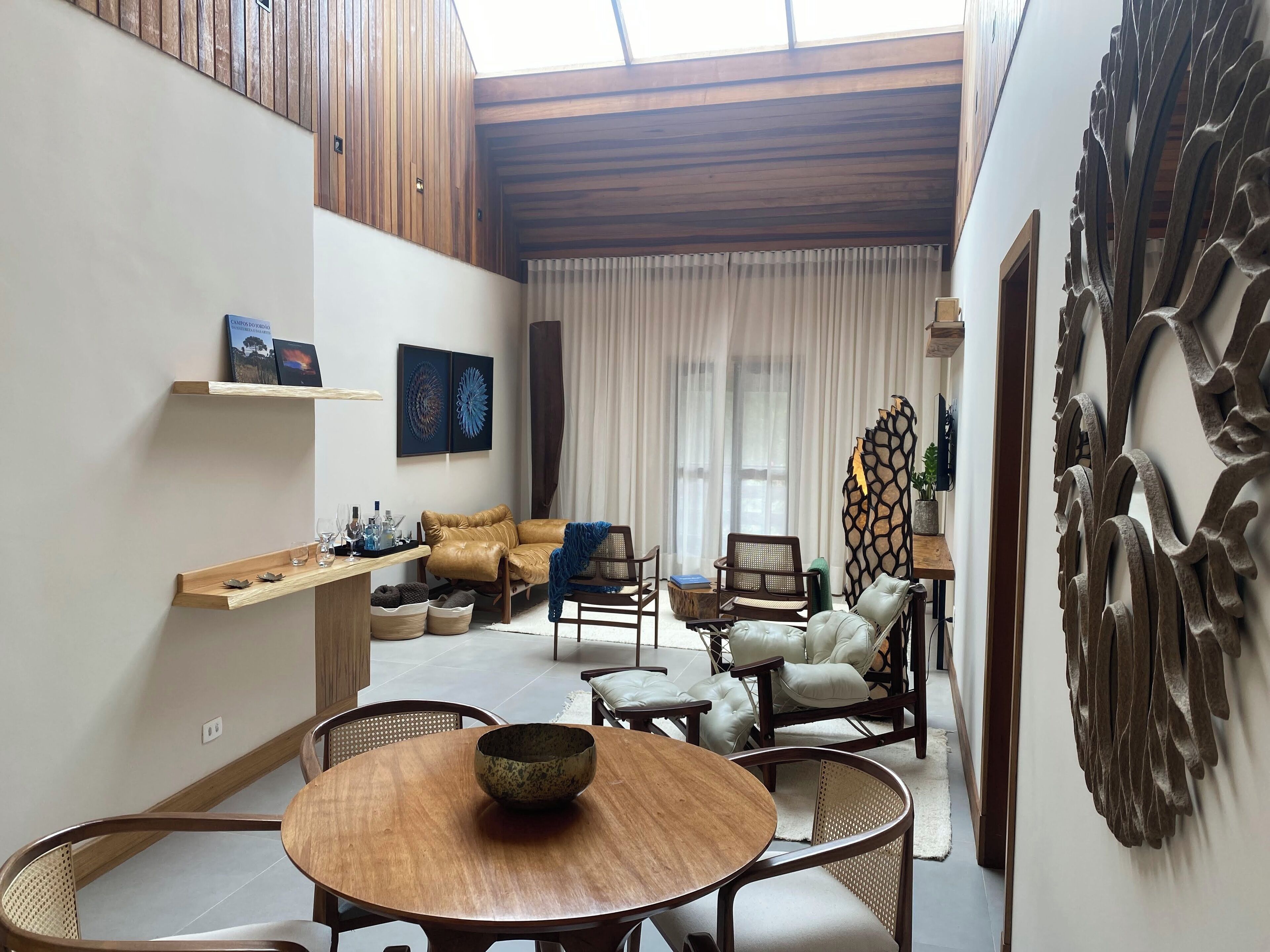 Uma sala de estar moderna com uma mesa redonda de madeira, sofás de couro e uma peça decorativa na parede.