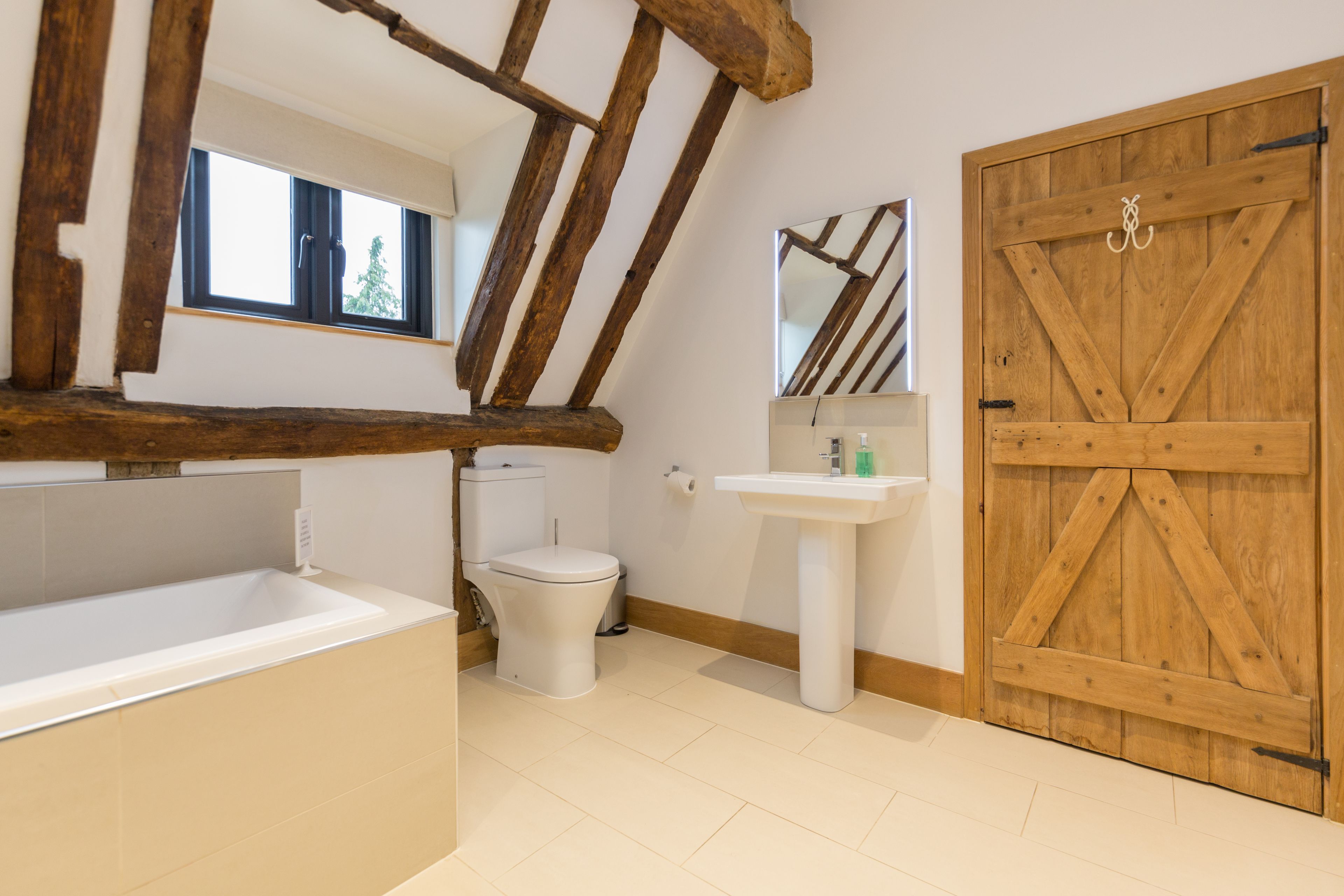 A bathroom with a bathtub, toilet, sink, wooden beams, and a large wooden door.