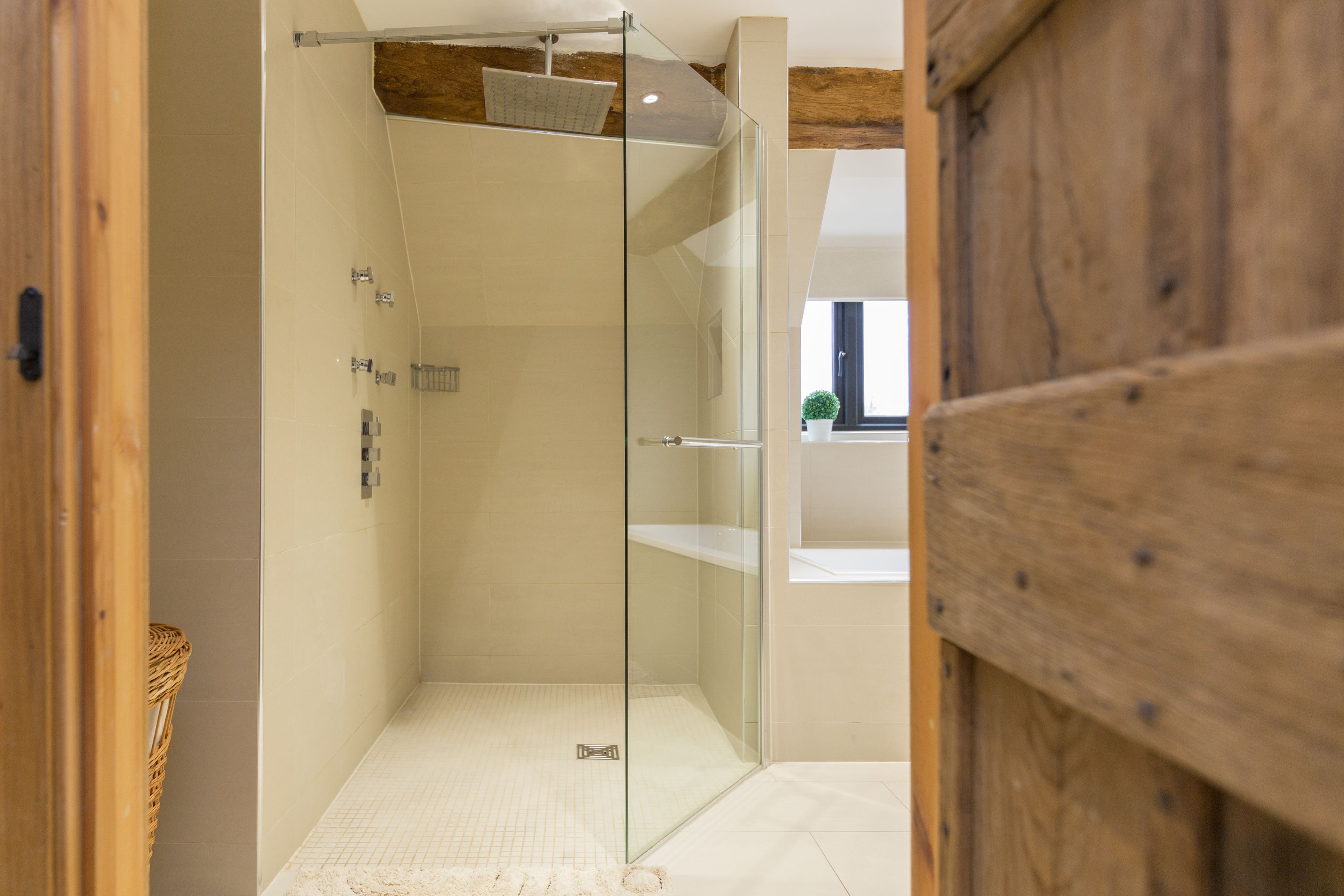 A modern bathroom with a glass-enclosed shower, wooden beams, and a white tiled floor.