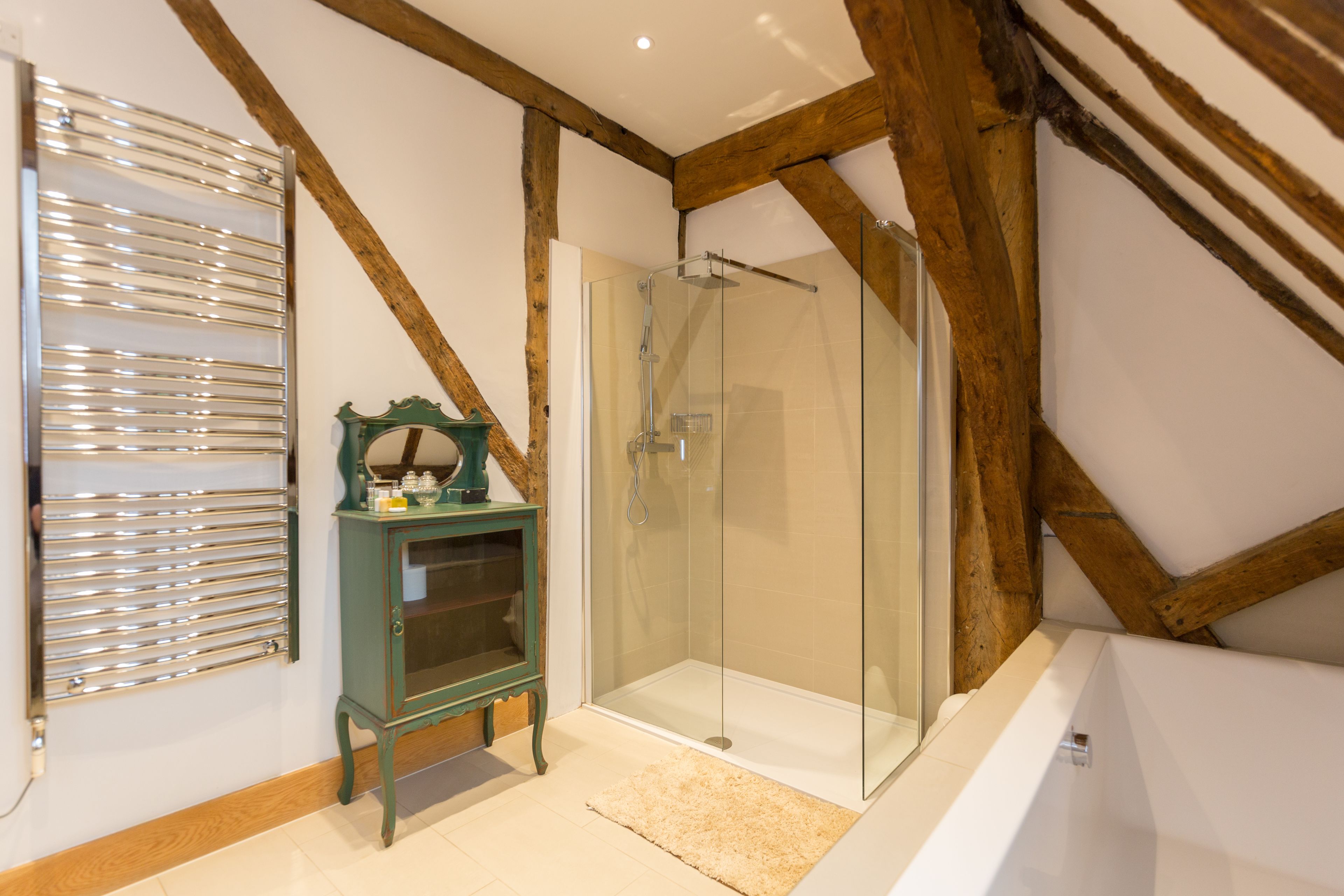 A modern bathroom with a glass shower enclosure, a wooden ceiling, and a small cabinet with decorative items.