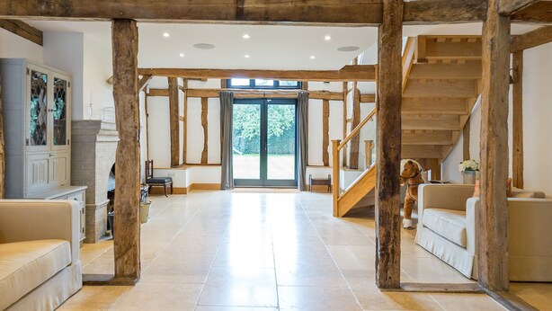 A spacious interior with a high ceiling, exposed wooden beams, a grand staircase, and a large open area leading to a glass door. - The Tithe Barn (Maidenhead)