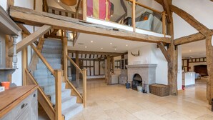 A spacious interior with a high wooden staircase, a fireplace, and a kitchen area. - The Tithe Barn (Maidenhead)