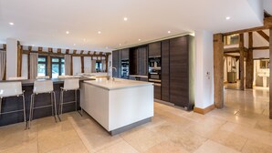 A modern kitchen with a central island, bar stools, and built-in appliances. - The Tithe Barn (Maidenhead)