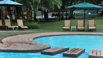 Uma área de piscina com espreguiçadeiras, um caminho curvo de tijolos e guarda-sóis.