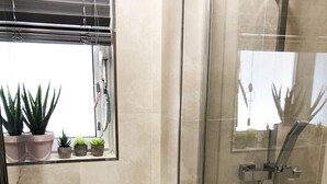 Ein Badezimmer mit einer einachigen Duschkabine, einem weißen Waschbecken und einem Fenster mit Topfpflanzen.