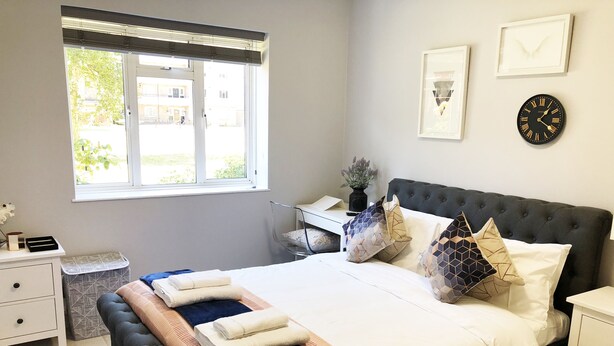 Ein Schlafzimmer mit einem Bett, Nachttischen, einem Fenster und einer Uhr an der Wand.