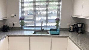 Eine Küche mit Spüle, Kaffeemaschine und Toaster. Auf der Fensterbank stehen Blumentöpfe und an der Wand ist eine Steckdose.