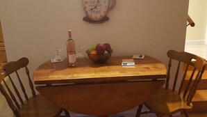 Ein Holztisch mit Stühlen, eine Obstschale, eine Flasche und ein Glas.