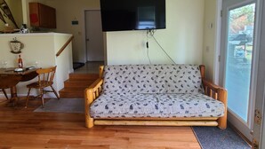 Ein Wohnzimmer mit einer Couch, einem Holzesstisch, Stühlen und einem an der Wand montierten Fernseher.