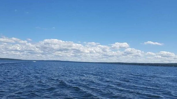 Blick auf ein großes Gewässer mit einer fernen Küstenlinie und einem teilweise bewölkten Himmel.