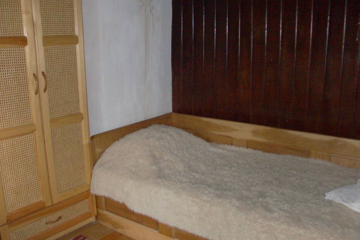 A room with a wooden bed, a white fluffy mattress, a wooden wardrobe, and a striped rug.