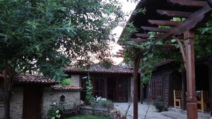 A rustic courtyard with stone pathways, a pergola, and a traditional building with a tiled roof. - Zarkovata Kashta (Kotel)