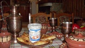 A dining table with traditional metalware, a jar of spread, and a television in the background. - Zarkovata Kashta (Kotel)