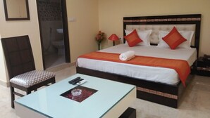 Une chambre d’hôtel comprenant un lit, une table avec un plateau en verre et une télécommande, une chaise et une petite table ornée d’un objet décoratif.