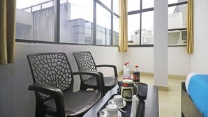 Une chambre d’hôtel avec deux chaises noires, une petite table sur laquelle se trouvent une bouteille, une tasse et une cuillère.