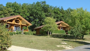 A lodge with two wooden cabins, surrounded by lush greenery and trees. - Village du Soleil (Mauroux)